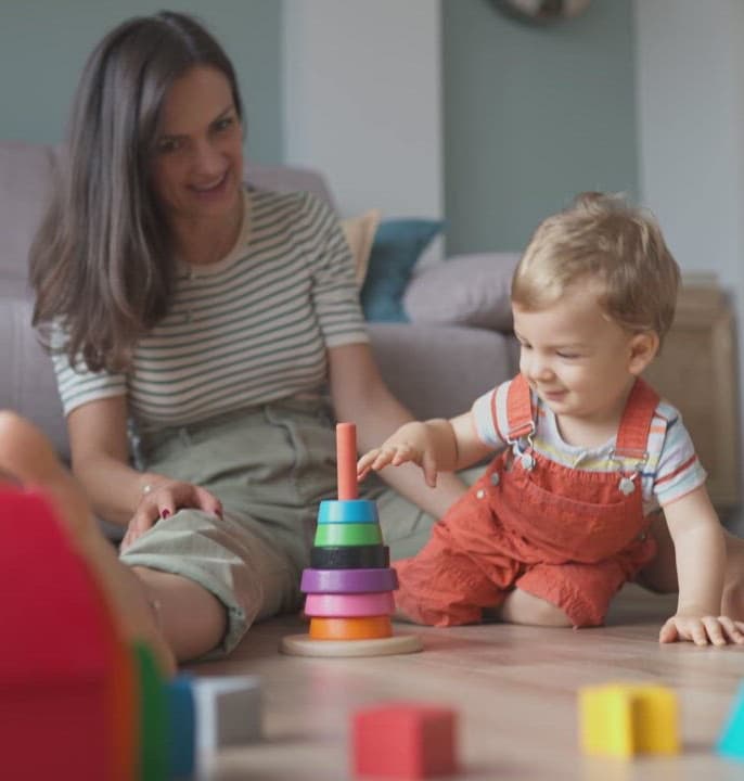 A toddler stacking rings with a grown-up on the living-room floor