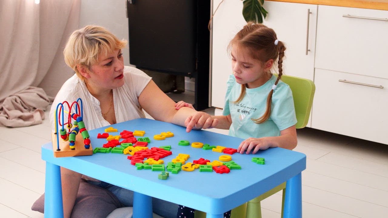 An Origin speech-language pathologist working on letters with a young girl at a table